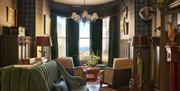 interior of communal lounge area at Portrush Adelphi which features various seating areas and large window which looks out towards the sea.