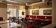 interior of Red Sails dining area at Portrush Adelphi which features red upholstered seating and chairs, with small lamps on every table.