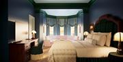 Elegant hotel room with a large bed dressed in cream linens and a tartan headboard. A pastel pink sofa sits in a bay window area with flowing blue cur