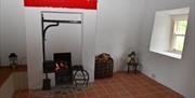 A woodburning fireplace in a tiled cottage with a window.