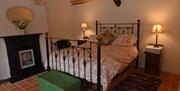 A tiled double bedroom with a fireplace, green storage chest and a rug.