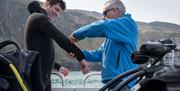 Man on a boat being assisted with his outfit by the guide as part of a scuba diving experience with Aquaholics