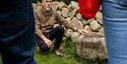 Instructor Mark kneeling beside a large stone on the Mourne Dry Stone Wall Building experience