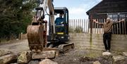 Man in a small digger moving large stones as part of the Mourne Dry Stone Wall Building experience with instructor Mark nearby