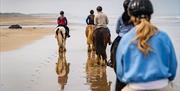 Group on horseback walking along the sand on the beach as part of the Saddle Up by the Sea experience with Crindle Stables