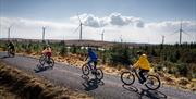 Group in single file on electric bikes on a trail with wind turbines in the background enjoying the Electric Escape experience with Corralea Adventure