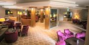 Lounge area of Ross Park Hotel with maroon and purple seating and dark wood tables.