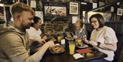 a group of 4 people enjoying food and drinks seated at table inside the bar.