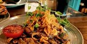 A plate of steak topped with crispy fried onions and microgreens, served with sautéed mushrooms and a grilled tomato. A pint of dark beer sits beside
