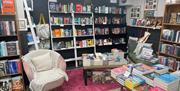 Pink seat with white rug and cushion surrounded by shelves and tables with books