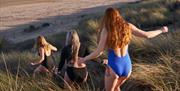 Three girls running down a sand dune to the sea