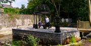 A man and woman resting under a canopy on a small manmade island in a garden.