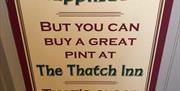 Wall sign reading 'You Can't Buy Happiness - But you can buy a great pint at The Thatch Inn - that's close enough!'