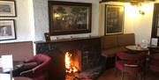 Downstairs bar in the Thatch Inn with open lit fire, pictures on wall and lounge tables with seats
