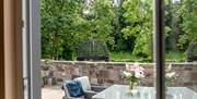 A view through a door of an outdoor stone seating area with garden furniture and a garden.