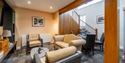 A lounge/dining area with a sofa, two chairs, a coffee table, a TV, a table & chairs and a staircase.