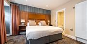 A double bedroom with bedside tables, curtains and a doorway to an en-suite.