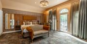 A large master bedroom with a mirror, sofa  and a door to an outdoor seating area.
