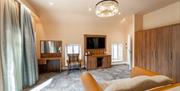 A large double bedroom with a makeup table, chair, TV, sofa and a large wardrobe.