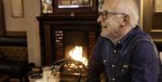 male sitting at a table in front of fire bar with a drink and the paper