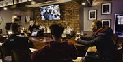 3 males sitting at bar watch TV with barman pulling at pint.