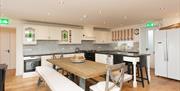 Kitchen dining area with a full kitchen, table with chairs and benches and a double door refrigerator.