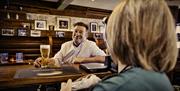 male seated at bar with barmaid drying glass