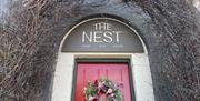 Archway over red door with sign reading The Nest and garland on the door