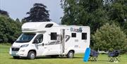 Image of a persons hand holding a coffee cup. The person is lying on their stomach on a bed. The bed is positioned on the roof of a Volkswagen camperv