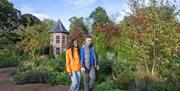 A couple walking on a garden path with lots of trees and other plants.