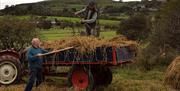 Two men manually loading sheaves of straw onto a vintage trailer