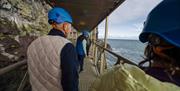 A group walks across a bridge over the open sea which swells at their feet