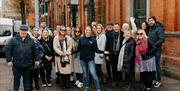 Group of guests on Belfast Food Tour standing outside St George's Market, smiling at camera in group shot with their tour guide