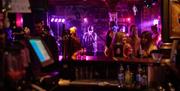A lively scene inside Jack's Bar with a performer singing on stage under colourful lights. Patrons are gathered around the bar, enjoying drinks and ch