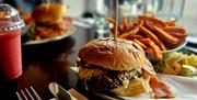 Close-up of a juicy cheeseburger with crispy bacon and caramelized onions, served with a side of sweet potato fries and a small salad on a plate. A be