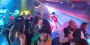 A lively scene at Jack's Bar featuring live entertainment. The dancefloor is packed with people enjoying the music under colourful lights. A disco bal
