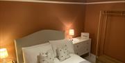 Double bed with white bed linen, terracotta walls and bedside lamps either side f the bed