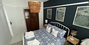 Downstairs bedroom with white iron framed double bed, blue bedding, white wooden floor and dark brown bedroom furniture