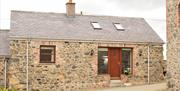 Image shows front of stone cottage with wooden door and gravel driveway.