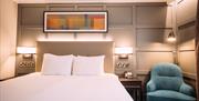 image of a hotel bedroom in the Crowne Plaza Belfast hotel. White linen, grey leather head boards, grey panelled walls. Blue sofa chair on the right.