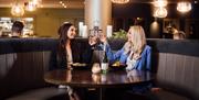 Two women having dinner inside the Green Room restaurant in the Crowne Plaza Belfast hotel. They are sat at a semi-circle booth, there is warm lightin
