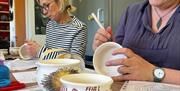 people sat at a table create designs on ceramic pots