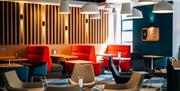 Photo of the open lobby in Holiday Inn Express Belfast City. Booths with colourful seating, colourful chairs and tables, wood panelled back wall and m