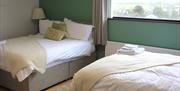 Jacaranda Room with two double beds featuring a sage green feature wall with matching cushions and throws.