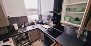 Kitchen with sink, washing machine, dishwasher, hob/oven and a cupboard with green crockery.