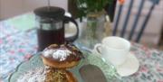 Kitchen table with display of pastries, coffee pot and vase of flowers