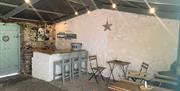 A barn converted into a bar area with garden furniture, barstools and lights.