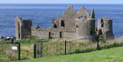 The photo is of Dunluce Caste. The Castle is old and run down.  The sea is in the background. A green field is in the foreground.