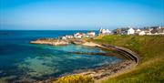 Panoramic view of Portballintrae bay, blue sea to the mid and fore on the left, green embankments on the right with harbour buildings and houses centr