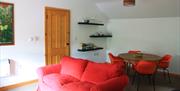 A sitting/dining area with a red sofa, a table with chairs and shelves for glasses, crockery and books.